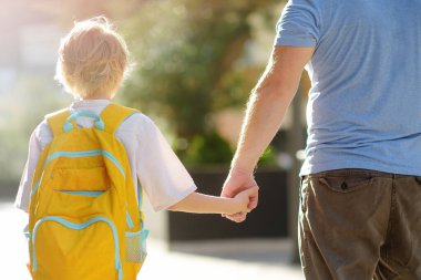Little schoolboy with his father goes to school after summer holiday. Parent accompanies or meets the child. Quality education for children. Kids back to school concept.