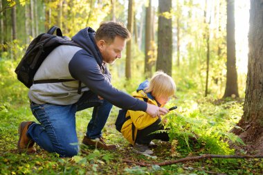 School boy and his father hiking together and exploring nature with magnifying glass. Little boy and dad spend quality family time in sunny forest of second summer. Daddy and little son. Fatherhood.