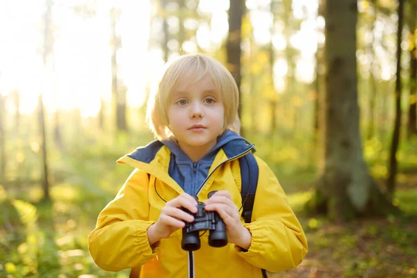 Little boy scout with binoculars during hiking in autumn forest. Child is looking with binoculars. Concepts of adventure, scouting and hiking tourism for kids. Exploring nature