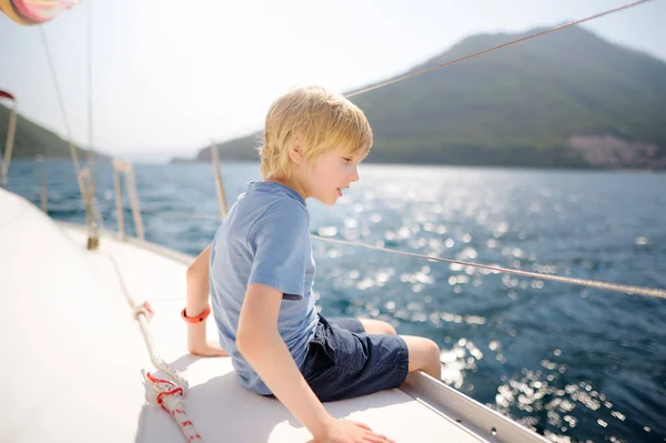 Little boy on board a sailing boat in the Boka Kotor Bay of the Adriatic Sea in the Balkan Mountains, Montenegro, Europe. Happy child on a sea trip during the sunny summer holidays day.