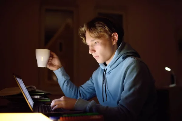 Concentrated teenager studying late night at home office with laptop and tablet. Modern technologies of remote working, distance learning, additional education, freelance