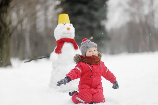大きな雪だるまと楽しい赤い服を着た小さな男の子 雪の冬の公園を散歩中の子供 子供連れの家族のためのアクティブな冬の屋外レジャー — ストック写真