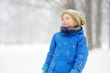 Küçük çocuk kar yağışında taze karla oynarken eğleniyor. Eldivenle kar tanelerini yakalayan bebek. Sıcak kıyafetler, şapka, eldiven ve eşarp giymiş bir çocuk. Çocuklar için açık havada aktif kış tatili