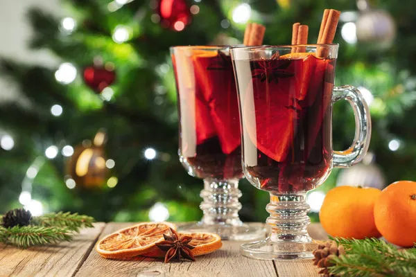 Dois copos de vinho ou gluhwein com especiarias e fatias de laranja na mesa rústica contra a árvore de Natal. Bebida tradicional em férias de inverno — Fotografia de Stock