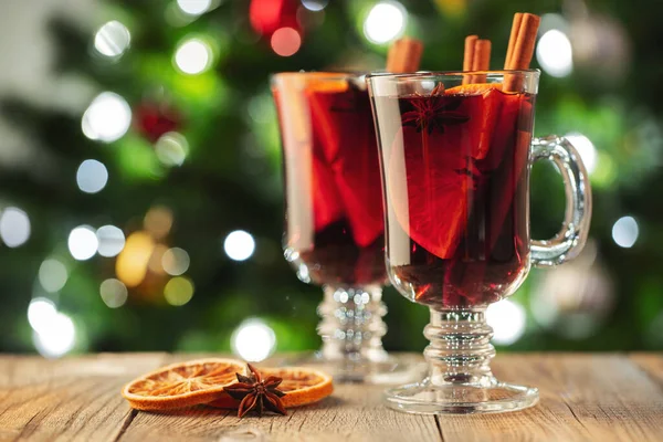 Két pohár karácsonyi forralt bor vagy gluhwein fűszerekkel és narancsszeletekkel a rusztikus asztalon a karácsonyfának támasztva. Hagyományos ital a téli szünetben — Stock Fotó