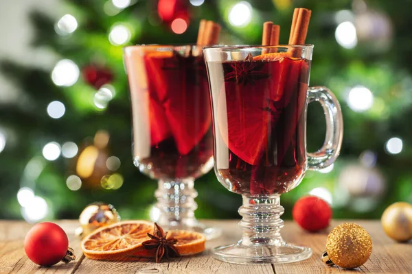 Zwei Gläser Glühwein oder Glühwein mit Gewürzen und Orangenscheiben auf dem rustikalen Tisch vor dem Weihnachtsbaum. Traditionelles Getränk im Winterurlaub — Stockfoto