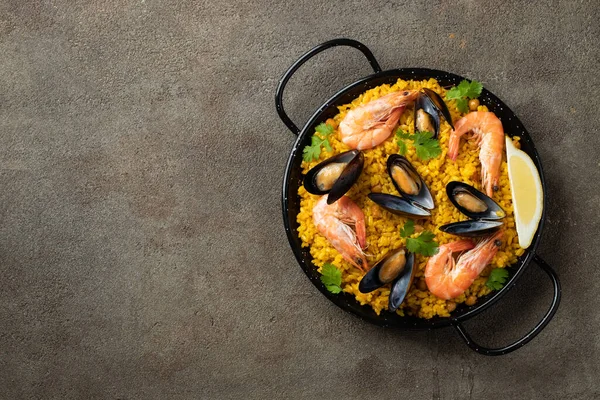 Paella tradicional española de mariscos en sartén con garbanzos, camarones, mejillones, calamares sobre fondo de hormigón marrón. Vista superior con espacio de copia — Foto de Stock