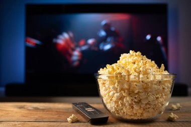 Bir cam kase patlamış mısır ve Uzaktan Kumanda Tv arka planda çalışır. Akşam rahat bir film veya Tv dizisi evde izlerken.