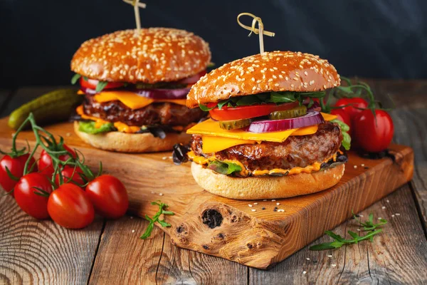 Dos deliciosas hamburguesas caseras de carne de res, queso y verduras sobre una vieja mesa de madera. Comida grasa poco saludable de cerca — Foto de Stock
