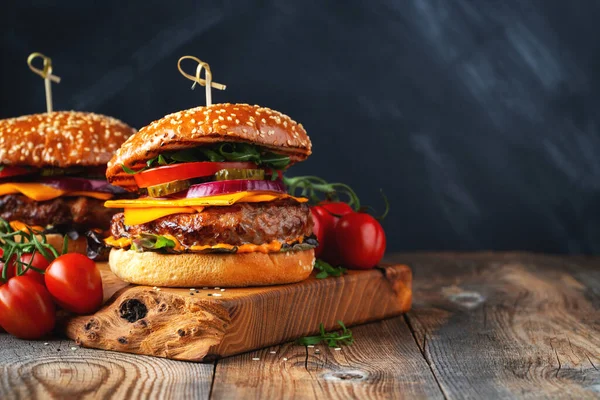 Dos deliciosas hamburguesas caseras de carne de res, queso y verduras sobre una vieja mesa de madera. Comida grasa poco saludable de cerca. Con espacio de copia — Foto de Stock