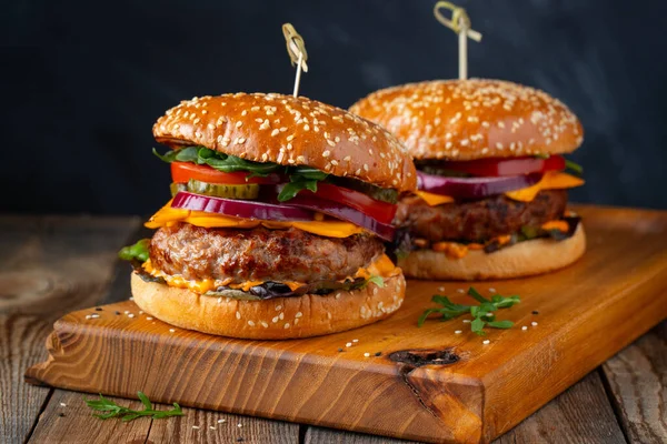 Dos deliciosas hamburguesas caseras de carne de res, queso y verduras sobre una vieja mesa de madera. Comida grasa poco saludable de cerca — Foto de Stock