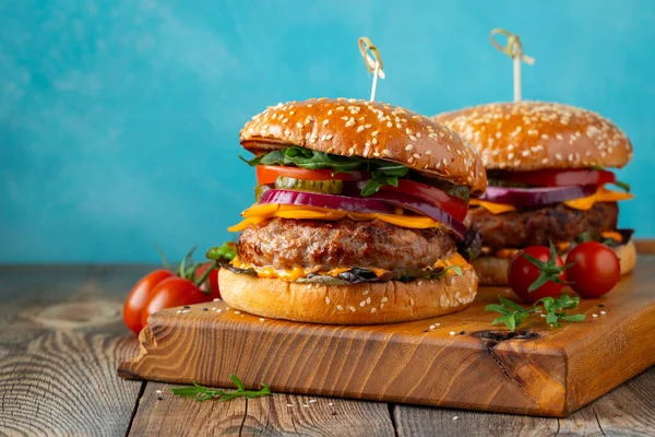两个美味的自制汉堡包，牛肉，奶酪和蔬菜放在一张古老的木制桌子上。脂肪不健康食品特写。有复制空间 — 图库照片