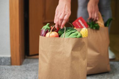 Bir kadın evinin kapısından bir torba yiyecek aldı. Coronavirus. Karantinaya alın. Evde kal, online alışveriş yap. Karantina ve kendini izole etme süresince sebze ve meyve teslimatı.