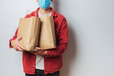 Koruyucu maskeli genç teslimatçı elinde kağıt torbalarla. Alışveriş çantalı bir kurye. Süpermarketten eve güvenli teslimat. COVID-19 koronavirüs koruması
