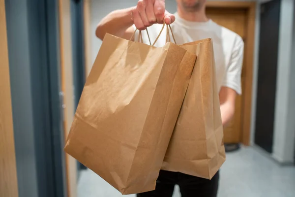 Delivery man holding paper bag with food in the entrance. The courier gives the box with fresh vegetables and fruits to the customer