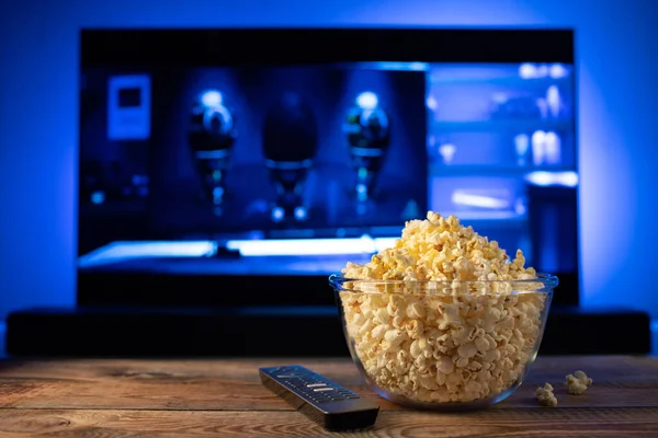 Szkła miskę popcorn i zdalnego sterowania w tle telewizor działa. Przytulny wieczór, oglądając film lub serial Tv w domu — Zdjęcie stockowe