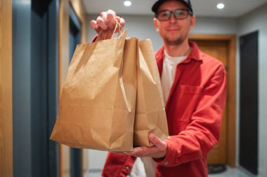 Paket teslimatçı girişte yiyecek dolu kağıt torba tutuyor. Kurye kutuya taze sebze ve meyve koyar..