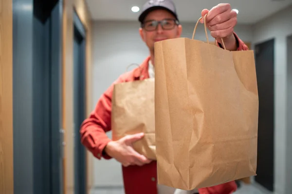 Delivery man holding paper bag with food in the entrance. The courier gives the box with fresh vegetables and fruits to the customer.