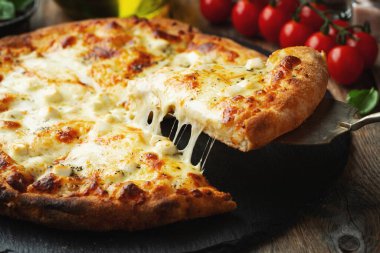 A slice of hot Italian pizza with stretching cheese. Pizza four cheeses with basil on a wooden background.