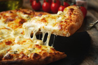 A slice of hot Italian pizza with stretching cheese. Pizza four cheeses with basil on a wooden background.