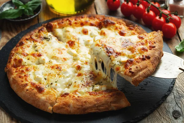 A slice of hot Italian pizza with stretching cheese. Pizza four cheeses with basil on a wooden background.
