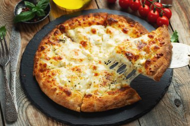 A slice of hot Italian pizza with stretching cheese. Pizza four cheeses with basil on a wooden background.