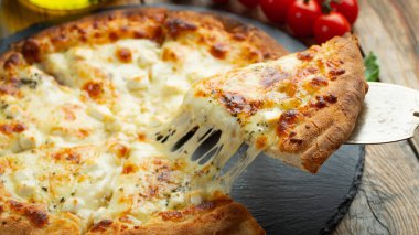 A slice of hot Italian pizza with stretching cheese. Pizza four cheeses with basil on a wooden background.