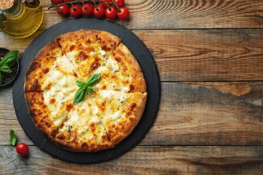 A slice of hot Italian pizza with stretching cheese. Pizza four cheeses with basil on a wooden background. Top view with copy space.
