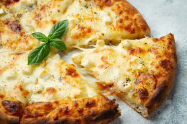 Italian pizza four cheeses with stretching cheese and basil on a light concrete background.