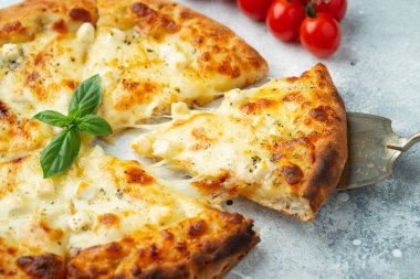 Italian pizza four cheeses with stretching cheese and basil on a light concrete background.
