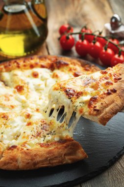 A slice of hot Italian pizza with stretching cheese. Pizza four cheeses with basil on a wooden background.