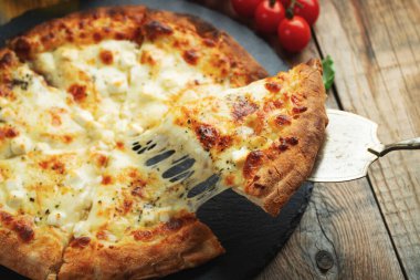 A slice of hot Italian pizza with stretching cheese. Pizza four cheeses with basil on a wooden background.