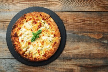 A slice of hot Italian pizza with stretching cheese. Pizza four cheeses with basil on a wooden background. Top view with copy space.