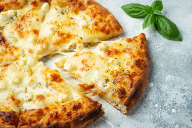 Italian pizza four cheeses with stretching cheese and basil on a light concrete background.