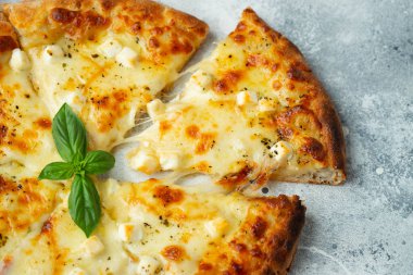 Italian pizza four cheeses with stretching cheese and basil on a light concrete background.
