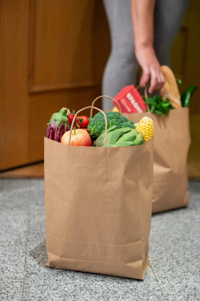 A woman picks up a bag of food at the door of her house. Coronavirus. Quarantine. Stay at home, Online shopping. Vegetables and fruits delivery during quarantine and self-isolation.