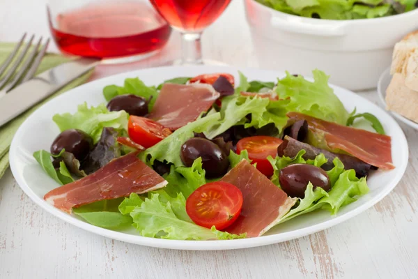 Salad with prosciutto, tomato and olives on the plate — Stock Photo, Image