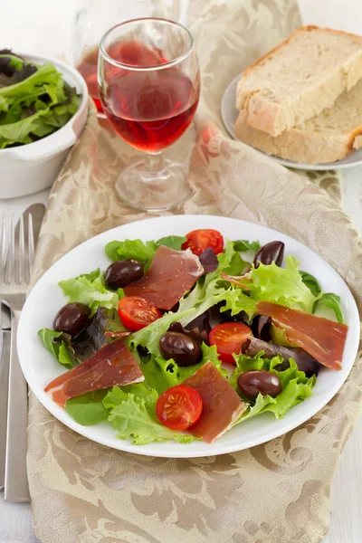 Salad with prosciutto, tomato and olives on the plate — Stock Photo, Image