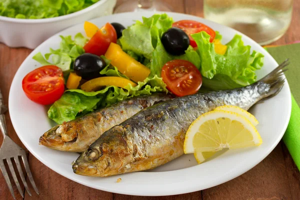 Sardinas fritas con ensalada y limón en el plato — Foto de Stock