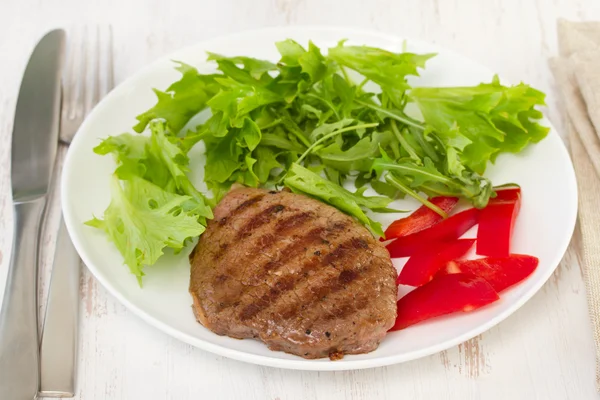 Carne grelhada com alface na placa branca — Fotografia de Stock