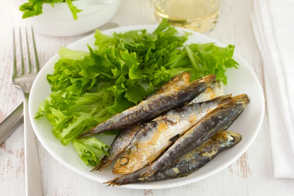 Smažené sardinky s salát na talíři — Stock fotografie