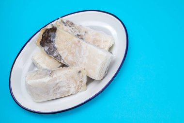 Mavi kağıtta beyaz tabakta donmuş morina balığı