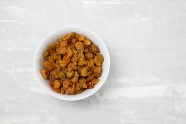 Seramik üzerinde küçük beyaz kasede kuru sarı üzümler.