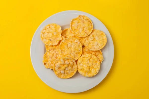small puffed corn cakes on small white plate on yellow paper