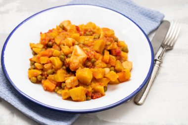 Gri seramik üzerinde beyaz tabakta sebzeli kalamar güveci.