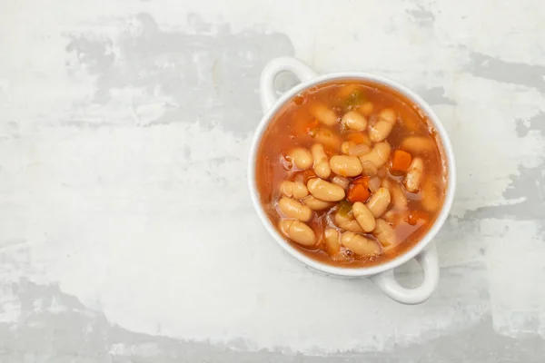 boiled white beans with vegetables and sauce on white bowl on ceramic