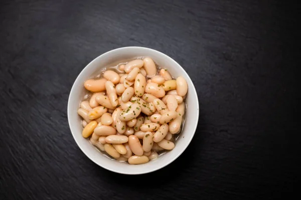 white beans with herbs in small white bowl on black ceramic