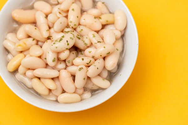 white beans with herbs in small white bowl on yellow paper