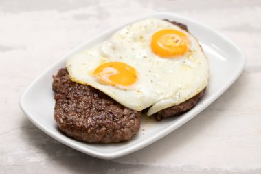 Üç kızarmış et ve beyaz tabakta kızarmış yumurta.