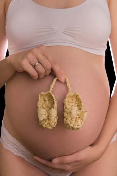 Little straw baby shoes on pregnant belly — Stock Photo, Image